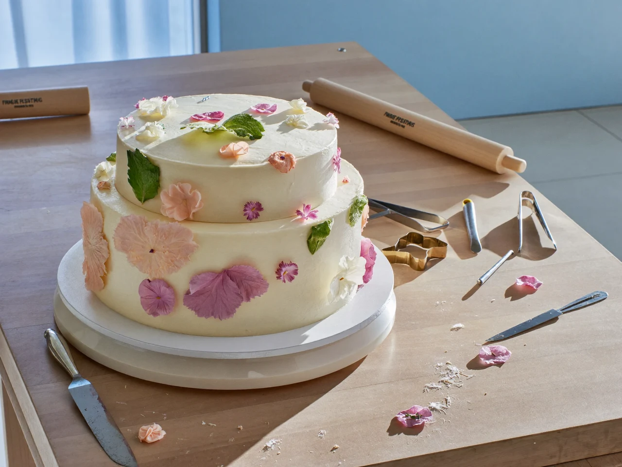 Illustrative sugarcraft workbench with a half-decorated tiered cake and scattered petals