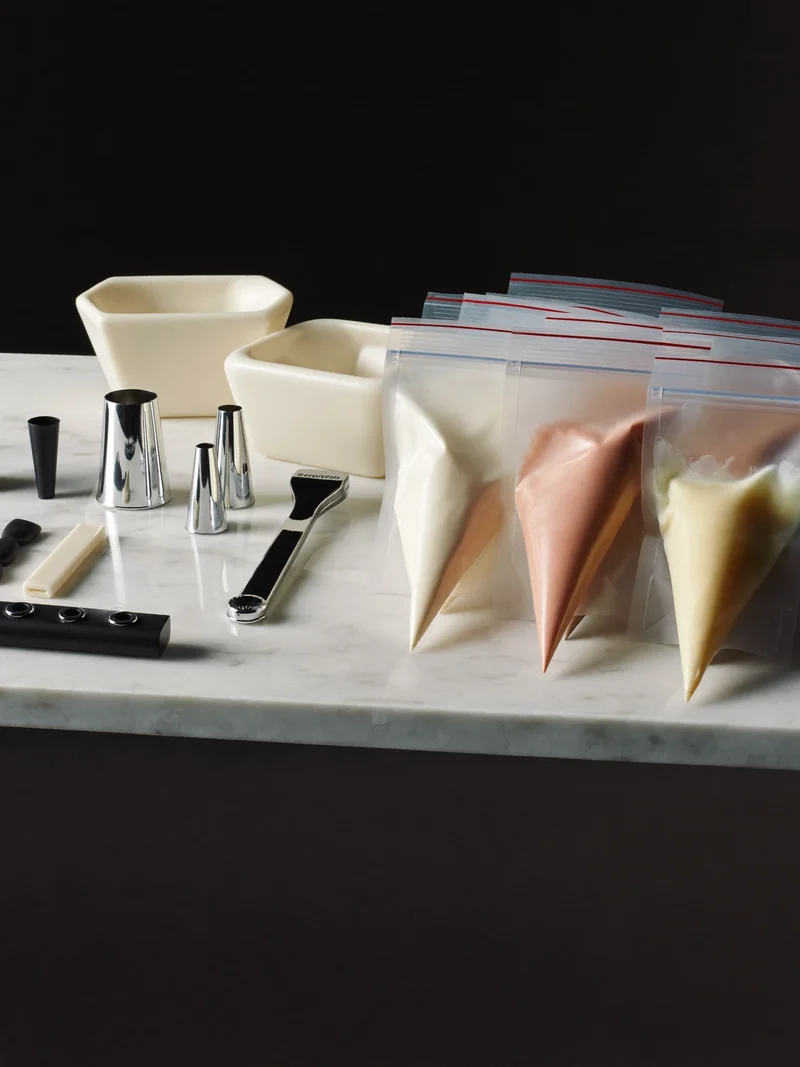 Illustrative silicone moulds, piping nozzles and filled bags on a marble slab