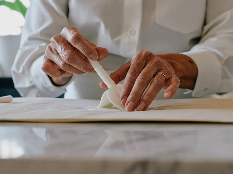 Illustrative hands shaping a sugar petal with a modelling tool at a bench
